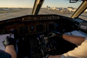 Hands adjusting airplane cockpit instruments with PSCG logo